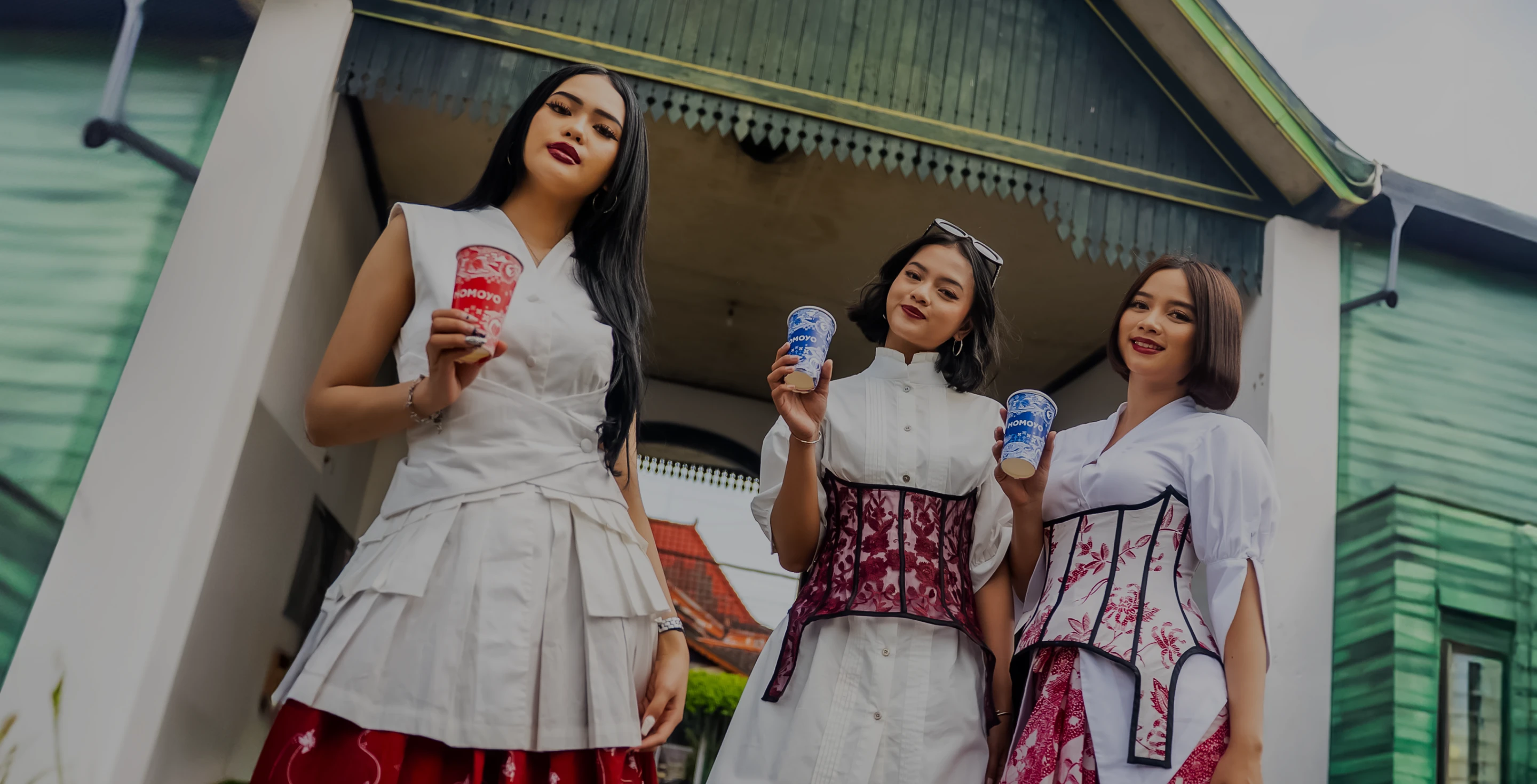 tiga perempuan yang berpose sambil memegang cup bertuliskan MOMOYO